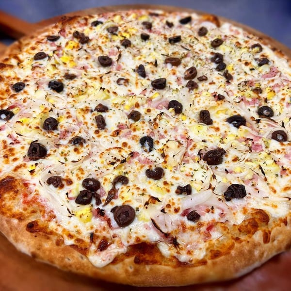 A Via Capri Pizzeria pizza with white sauce, cheese, ham, onions, and black olives.