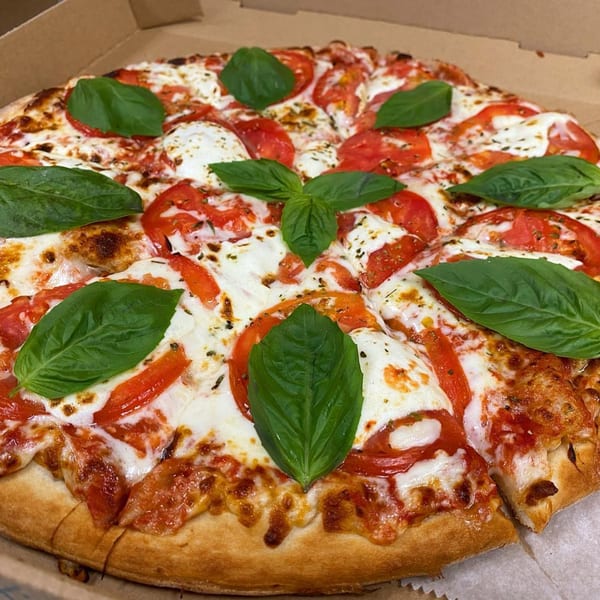 A freshly baked Via Capri Pizzeria Margherita pizza with basil leaves, tomatoes, and mozzarella cheese.